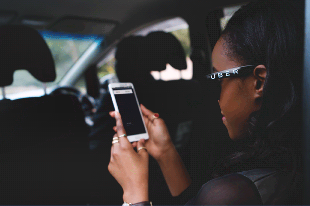 An Uber passenger in the rear seat of a car checking the status of her trip on her phone.